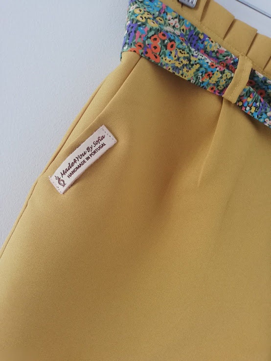 Calção artesanal de mulher em amarelo mostarda com pormenores de renda, cinto floral e efeito pregueado na cintura