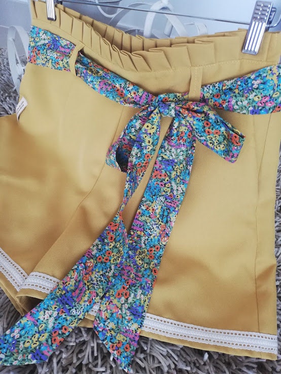 Calção artesanal de mulher em amarelo mostarda com pormenores de renda, cinto floral e efeito pregueado na cintura