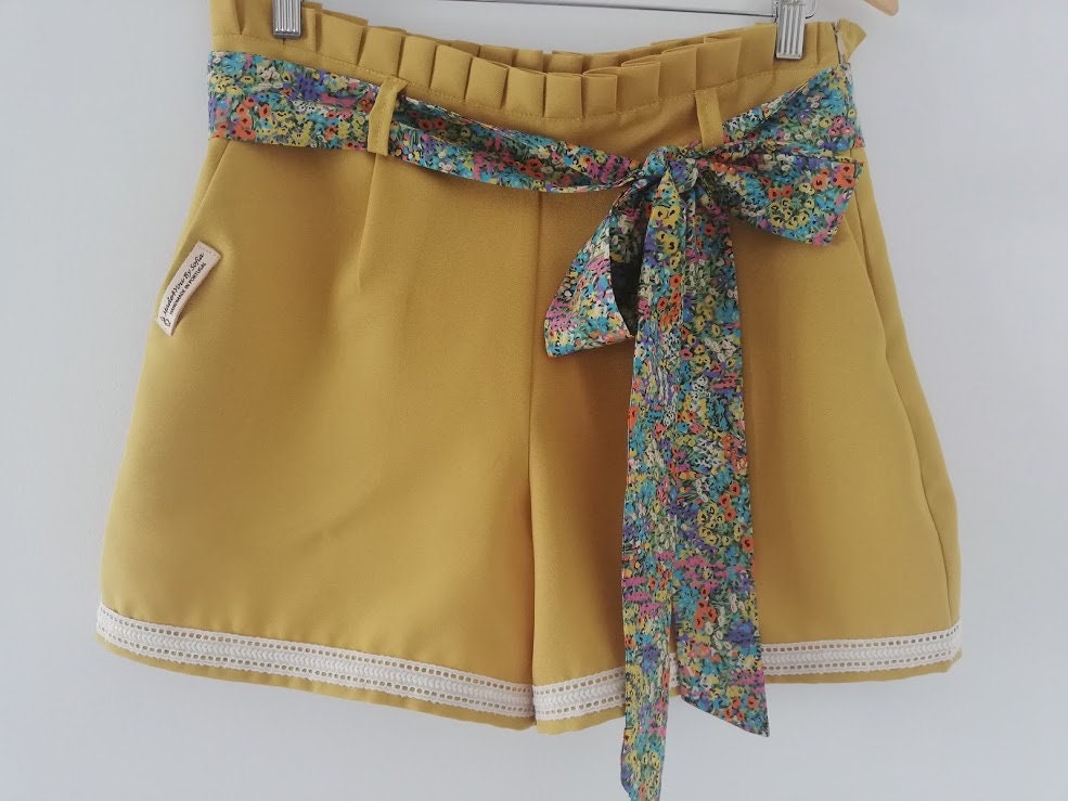 Calção artesanal de mulher em amarelo mostarda com pormenores de renda, cinto floral e efeito pregueado na cintura