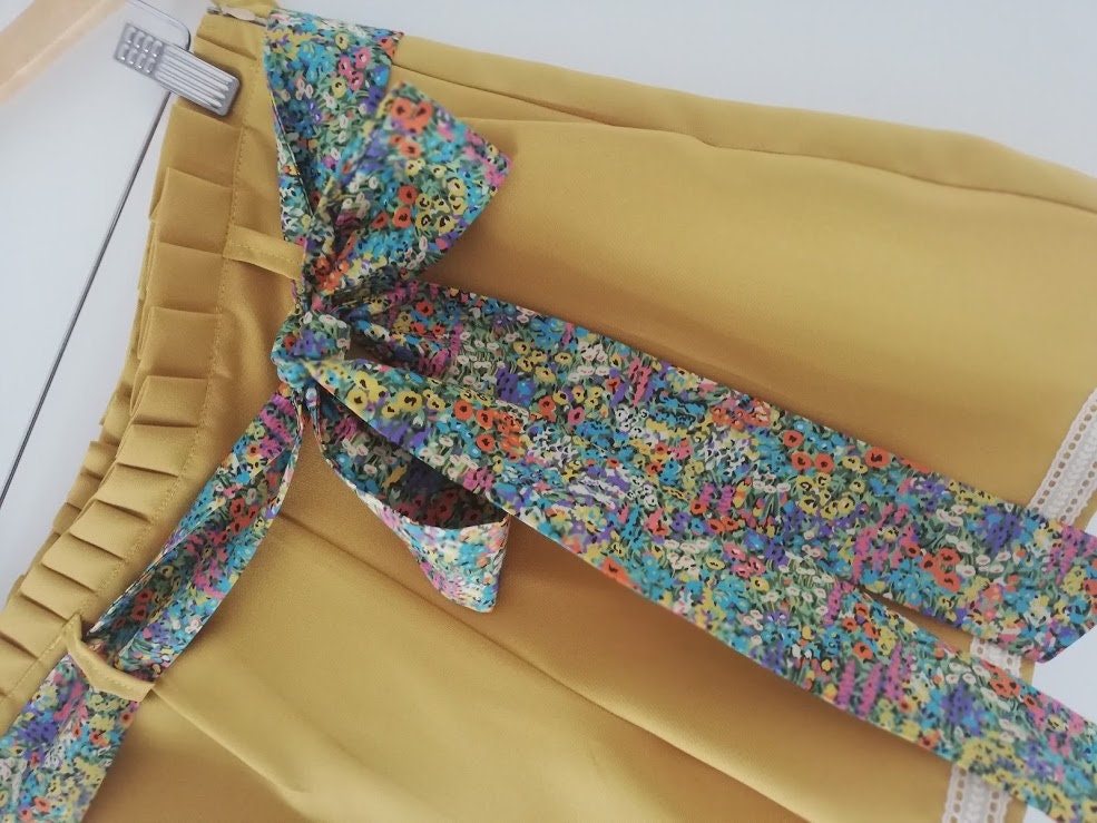 Calção artesanal de mulher em amarelo mostarda com pormenores de renda, cinto floral e efeito pregueado na cintura