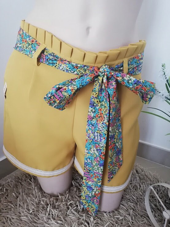 Calção artesanal de mulher em amarelo mostarda com pormenores de renda, cinto floral e efeito pregueado na cintura