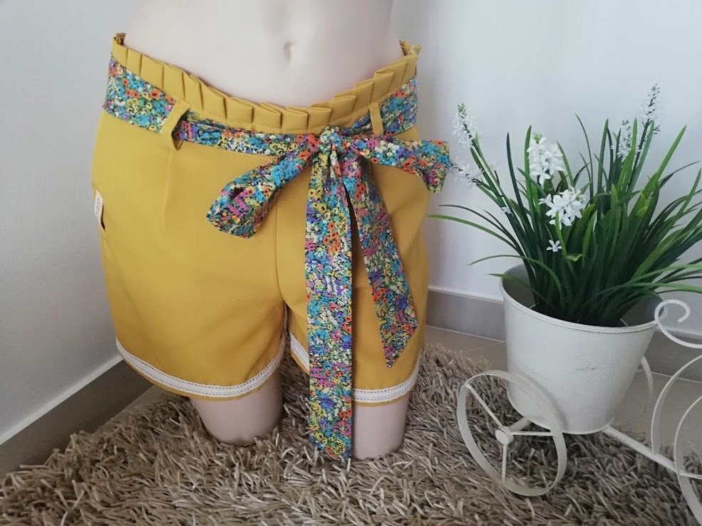 Calção artesanal de mulher em amarelo mostarda com pormenores de renda, cinto floral e efeito pregueado na cintura